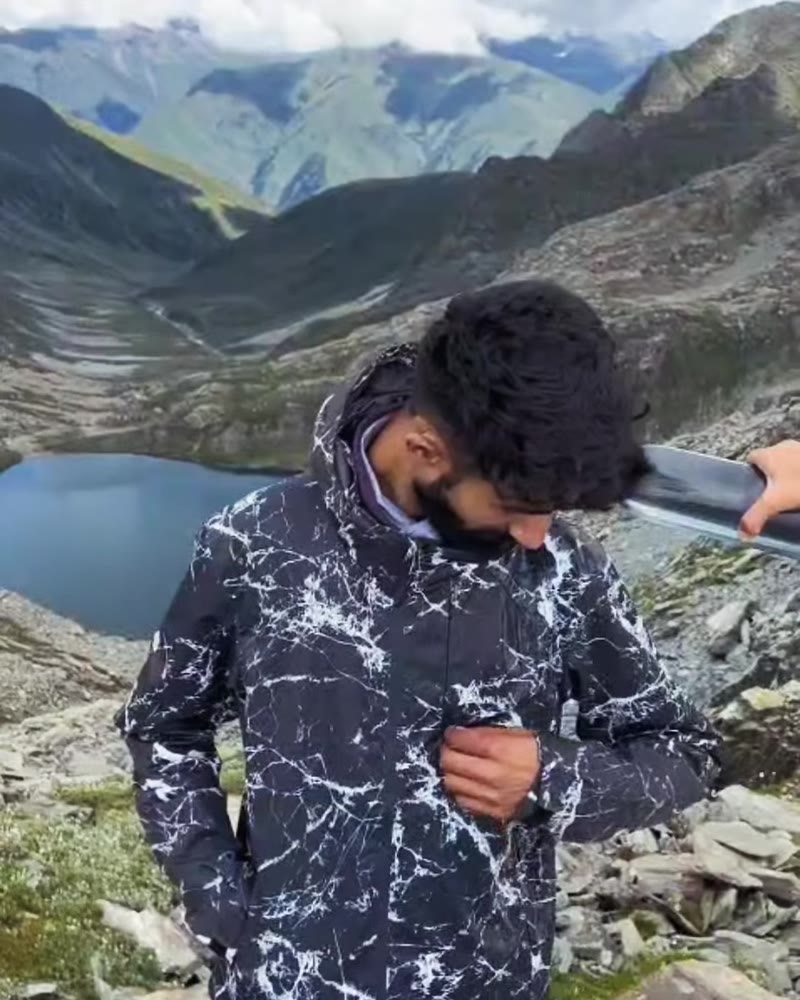 Man in a black and white marble-print hooded windcheater above a mountain lake in Kashmir