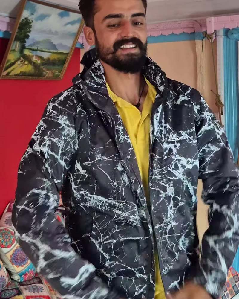 Man smiling in the marble-print windcheater indoors in a Kashmiri home
