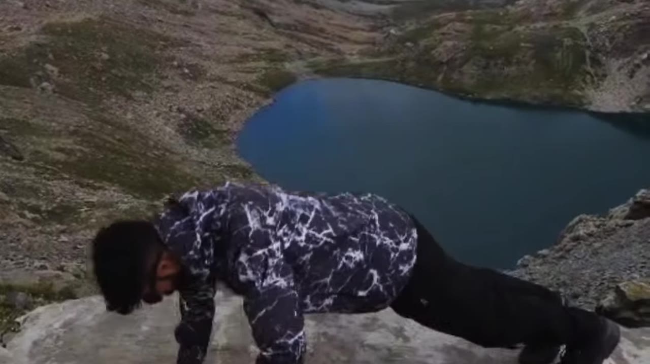 Hiker in the marble-print windcheater doing push-ups on a rock above a blue mountain lake