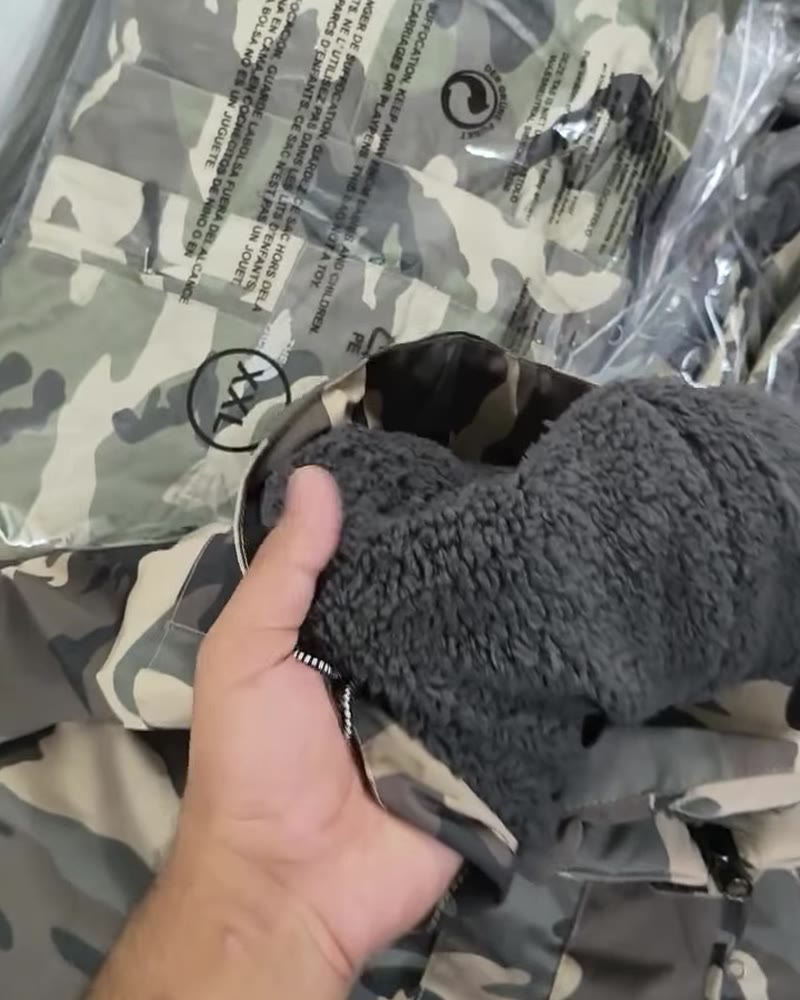 Hand opening a grey camo jacket to show the thick sherpa fleece lining